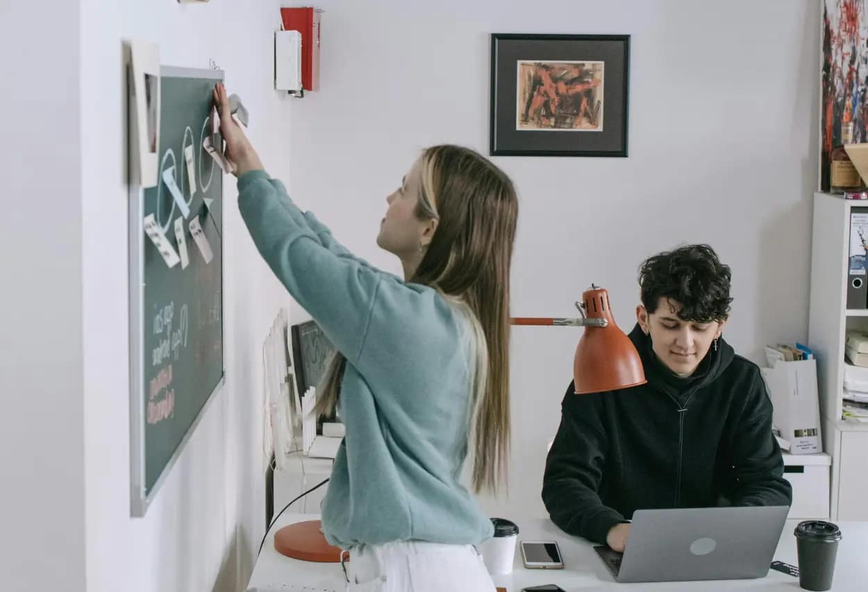 SEO consultant writing SEO strategies on a chalkboard while colleague analyzes data on a laptop, exemplifying the Eisenhower Matrix's principle of prioritization.