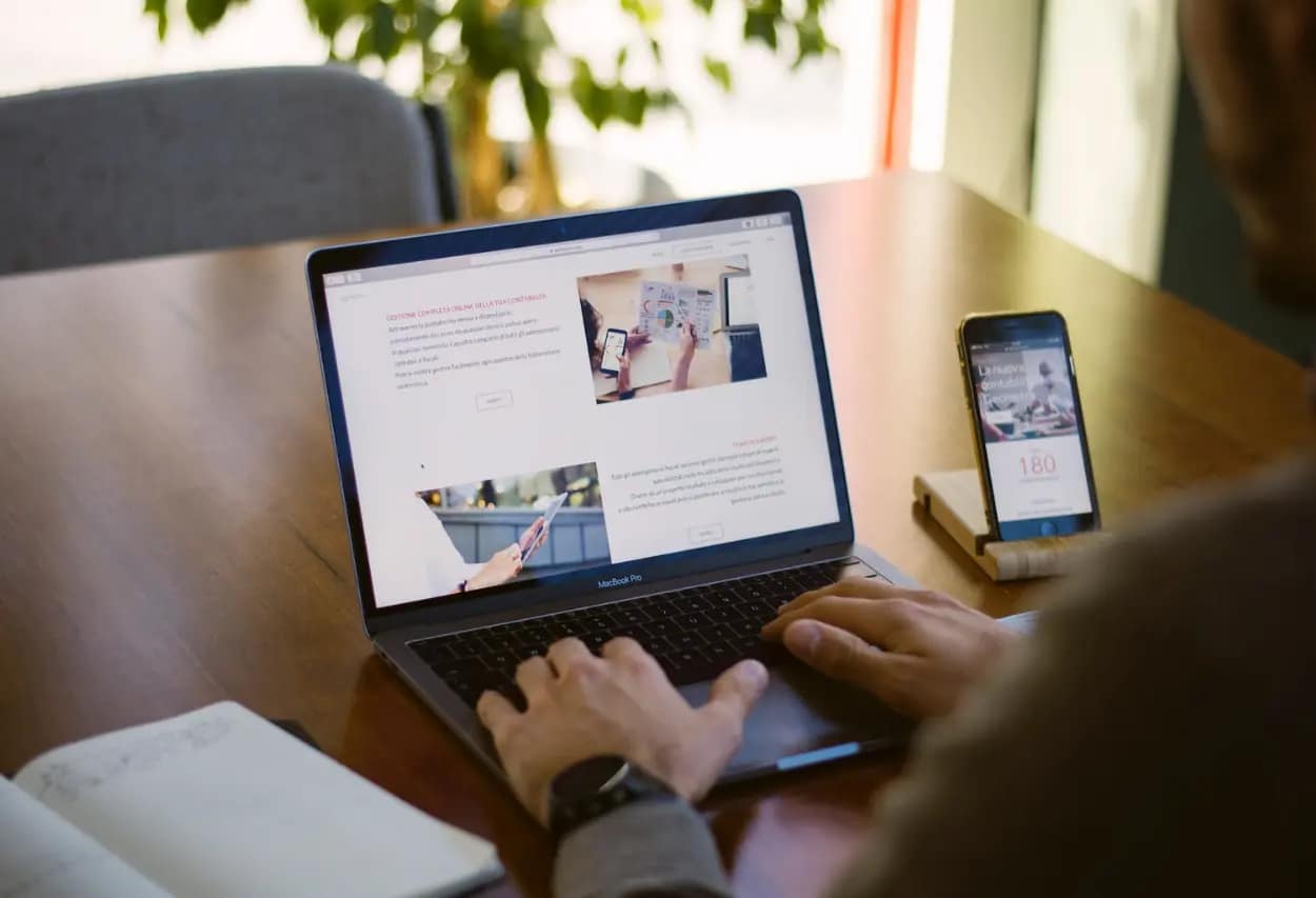 Man working on a MacBook Pro at a wooden desk with an iPhone and notebook beside him, displaying a website with custom guest posting creation services.
