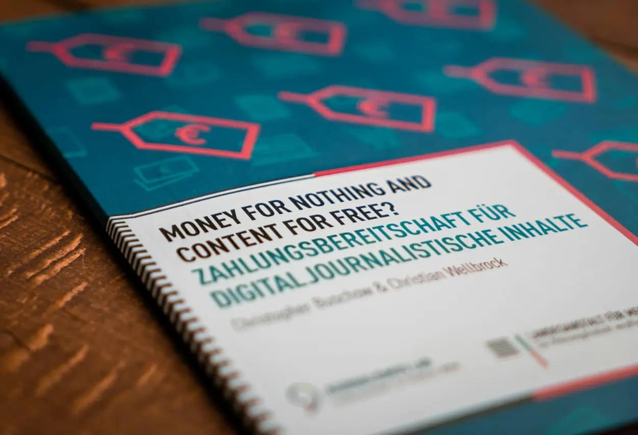 Close-up of a professional publication with the title 'Money for Nothing and Content for Free?' emphasizing digital journalism payment willingness, resting on a wooden surface