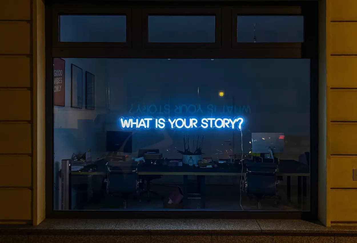 Office window reflecting 'What is your story?' neon sign, symbolizing the unique narratives of small businesses in local SEO.