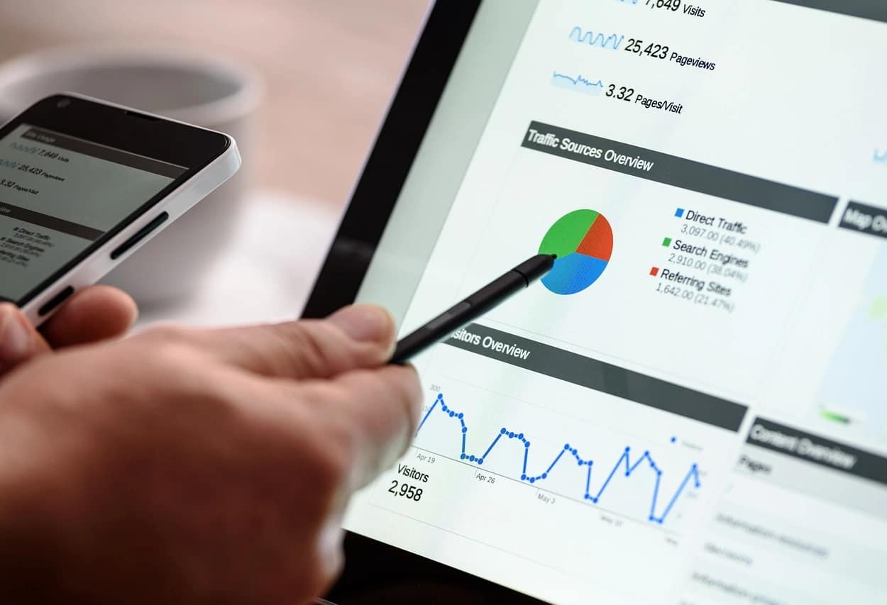 Hand holding a stylus pointing at SEO analysis on a tablet screen with data interaction on a smartphone