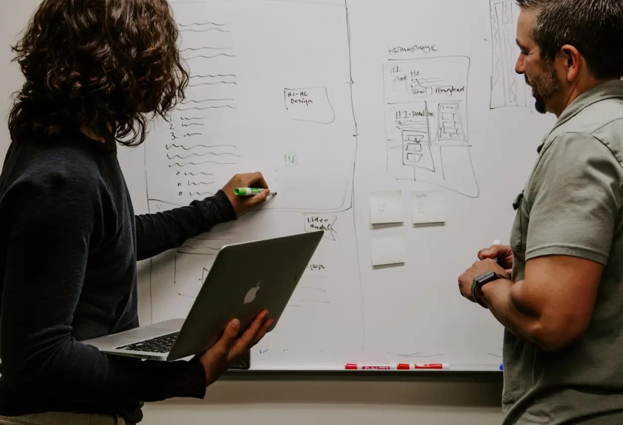 Web designers brainstorming on a whiteboard with a laptop, outlining the new site structure during a website migration.
