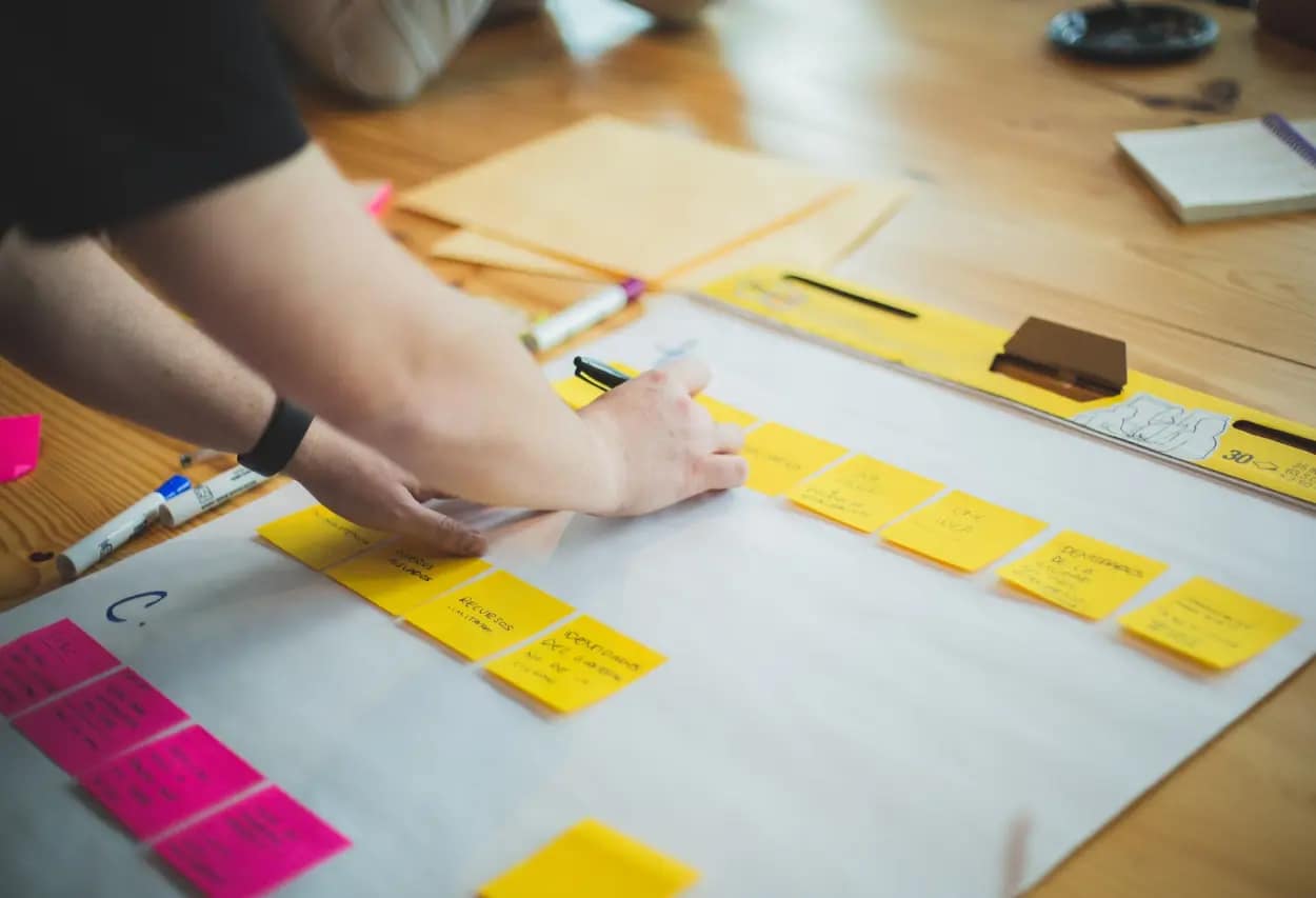 Hands organizing a workflow with yellow sticky notes on a whiteboard, planning for a comprehensive website migration strategy.