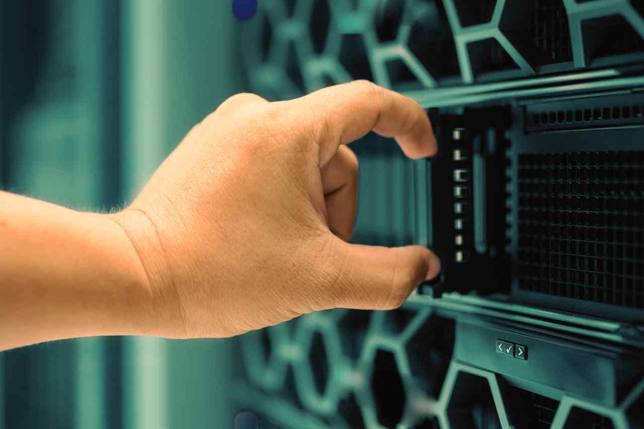 Close-up of a hand inserting or removing a server blade from a data center rack with a green and black honeycomb design, symbolizing eco-friendly and energy-efficient technology.