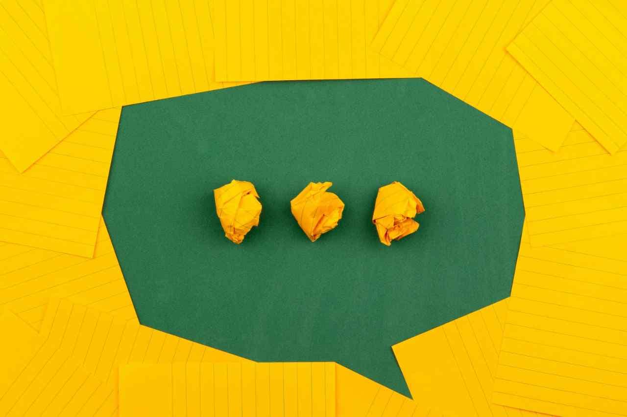 A conceptual image of a green speech bubble with crumpled yellow papers on a yellow background, representing the refinement of marketing ideas towards sustainable solutions.