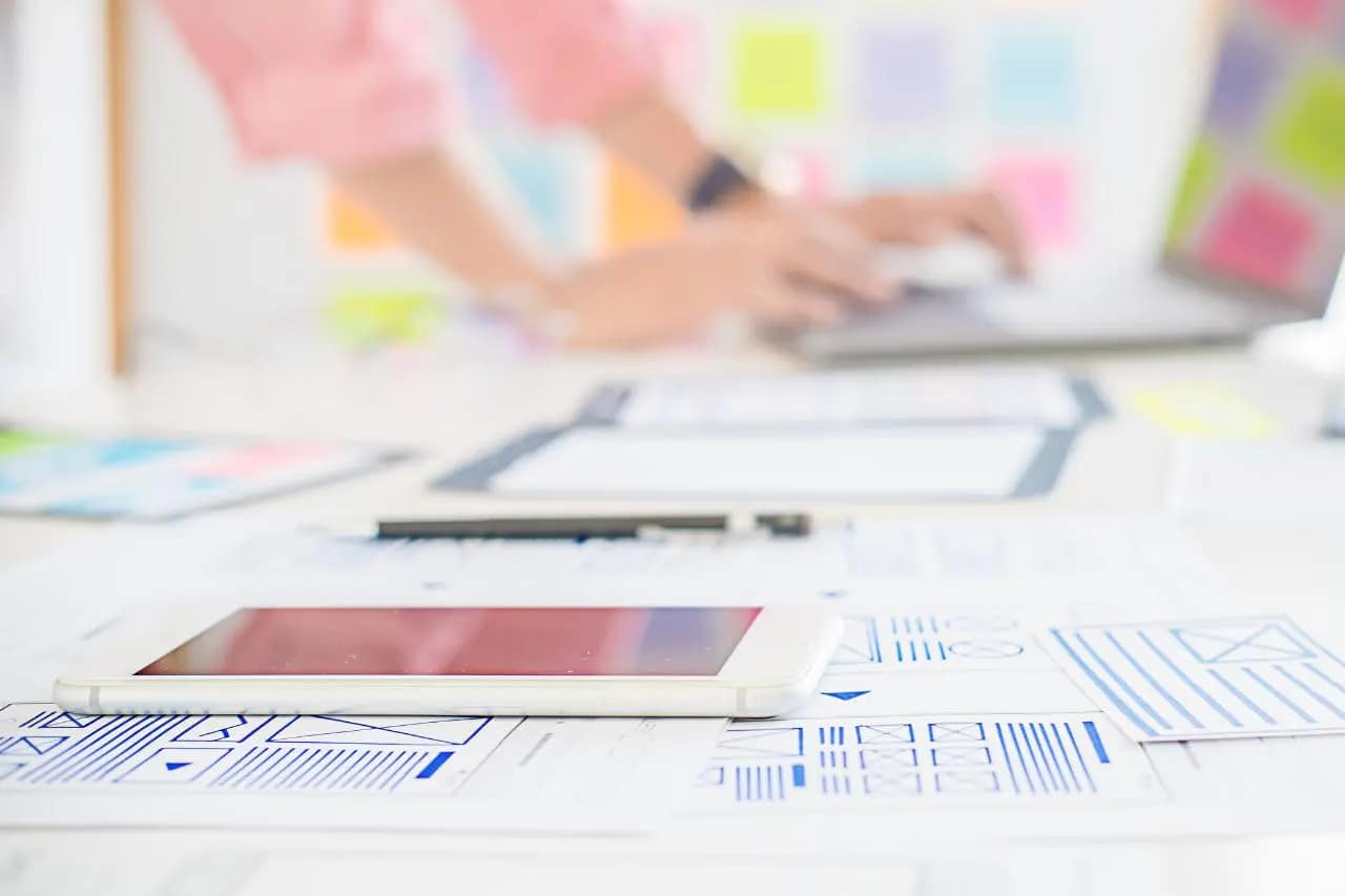 Blurry image of a web designer's workspace with wireframes and digital tablets, focusing on web accessibility in design layout.