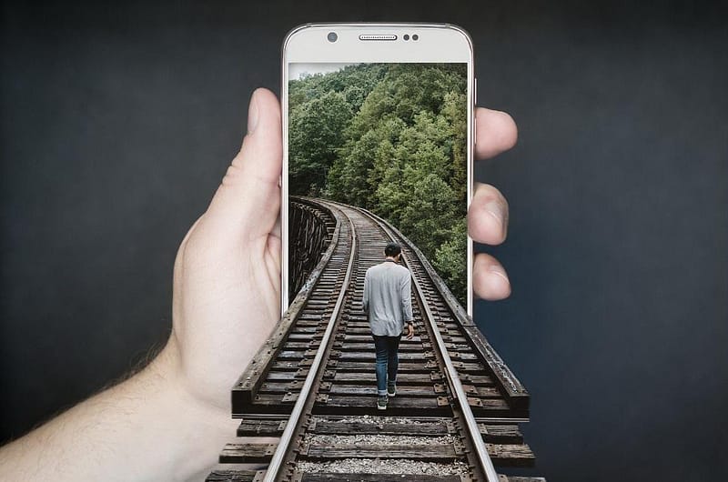 Innovative digital marketing concept with a man walking on railway tracks through a smartphone screen, symbolizing progressive paths in sustainable development.
